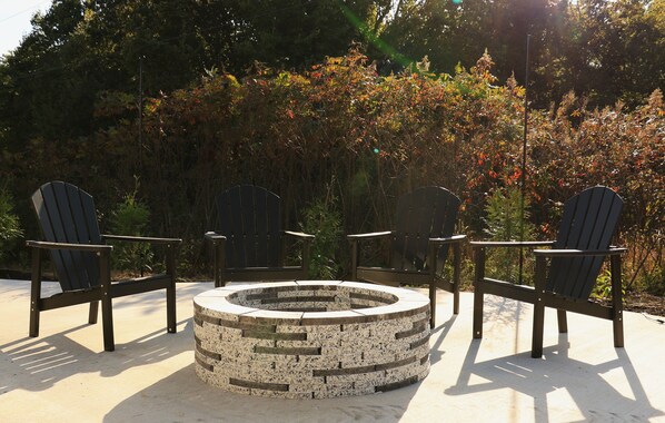 A circular stone fire pit surrounded by three Adirondack chairs in an outdoor setting.