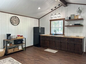 Una cocina con armarios de madera, un refrigerador negro, encimera de madera, un fregadero y una ventana con vistas.