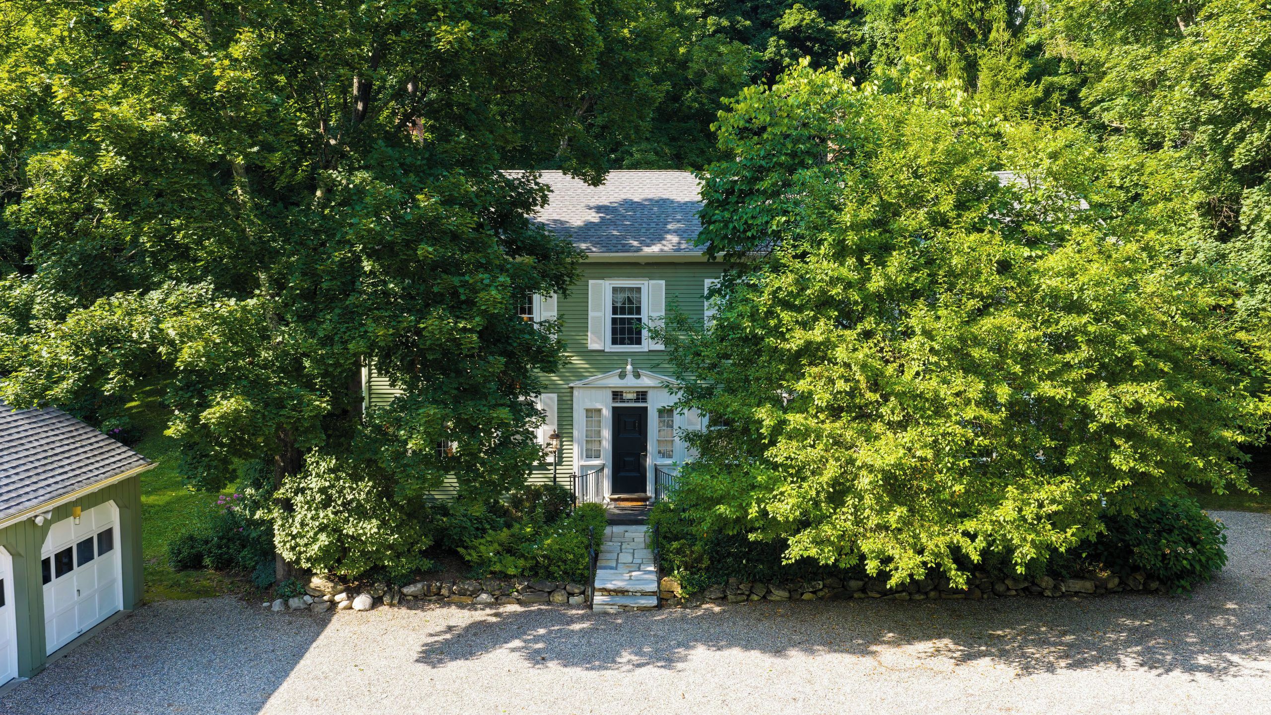 A two-story house with a front porch, surrounded by dense trees.