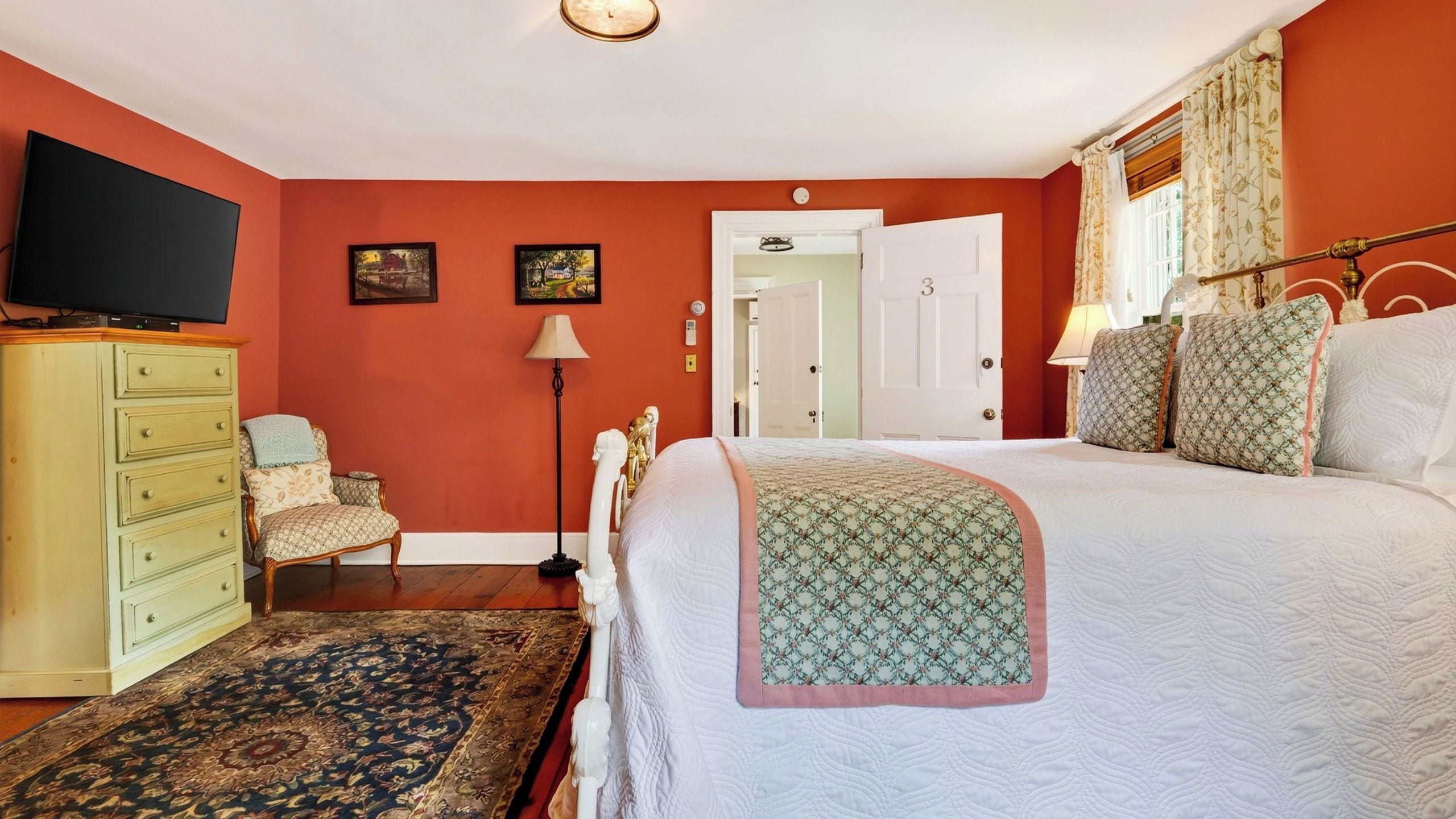 A bedroom with a bed, a dresser, a television, and a door leading to another room.
