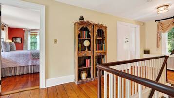 A room with a wooden floor, a large wooden bookcase, a bed with patterned bedding, and a white door.