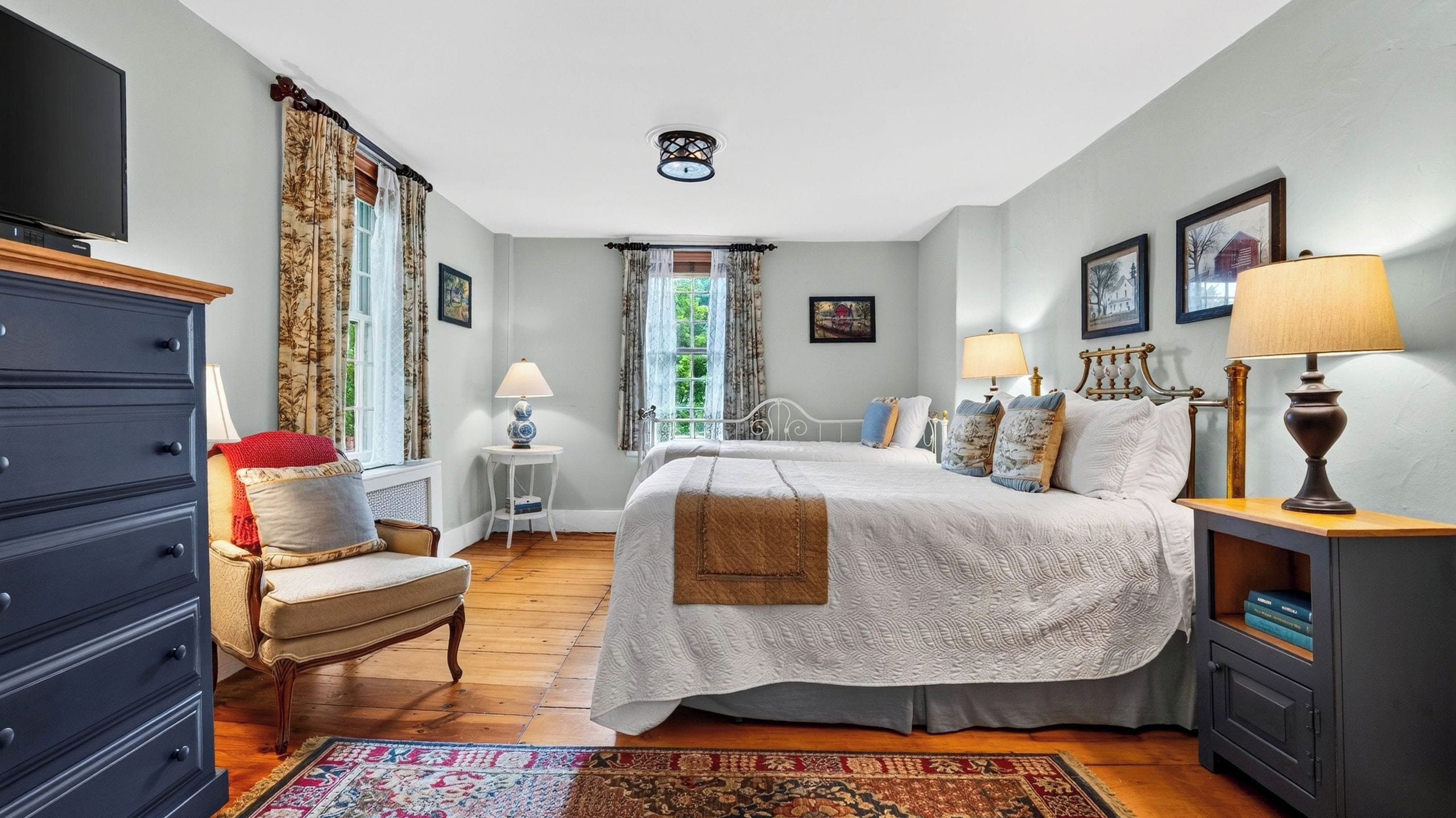 A bedroom with a bed, bedside lamps, a dresser, a chair, a small table, and a window with curtains.