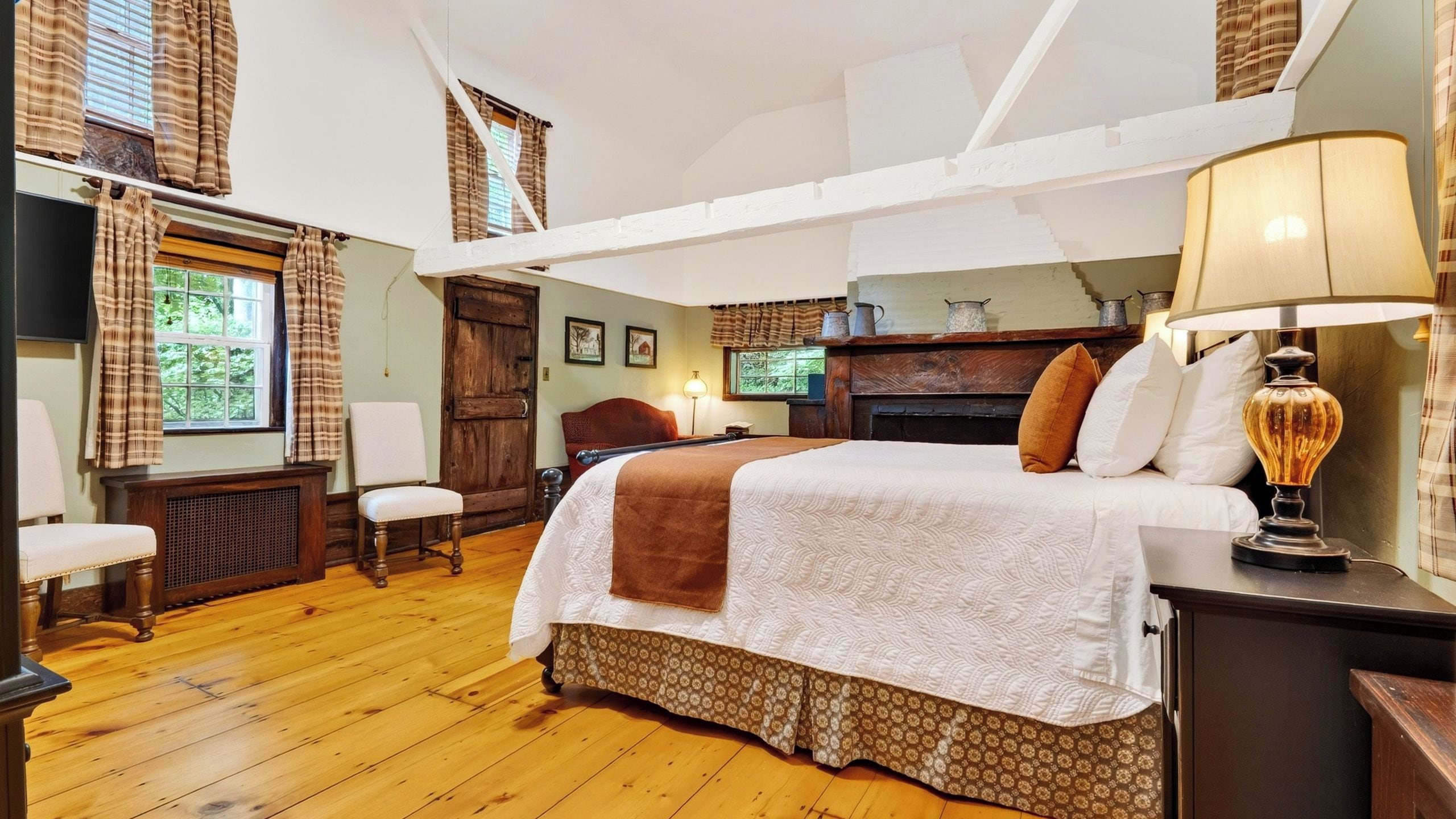 A bedroom with a large bed, a wooden chair, a desk, and a window with curtains.