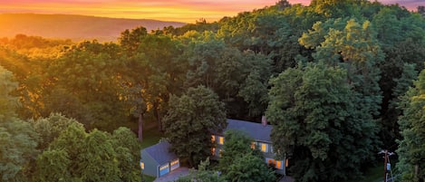 Un quartier résidentiel avec une maison entourée d’arbres denses, un ciel dégagé et une chaîne de montagnes lointaine.