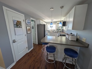 A modern kitchen with a central island, bar stools, pendant lighting, and a refrigerator. - Serene 2-bedroom lakeside waterfront cottage getaway in Michigan Center (Michigan Center)