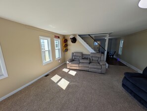A living room with a beige carpet, a gray sofa, and a staircase leading to another level. - Serene 2-bedroom lakeside waterfront cottage getaway in Michigan Center (Michigan Center)