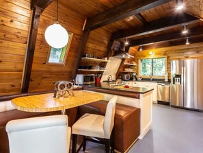 A cozy kitchen with a wooden interior, a dining area with a round table and cushioned chairs, and a built-in refrigerator.