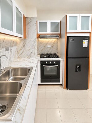 Une cuisine équipée d’un évier en acier inoxydable, d’une cuisinière noire, d’un réfrigérateur à deux portes et de meubles blancs avec des portes en verre.
