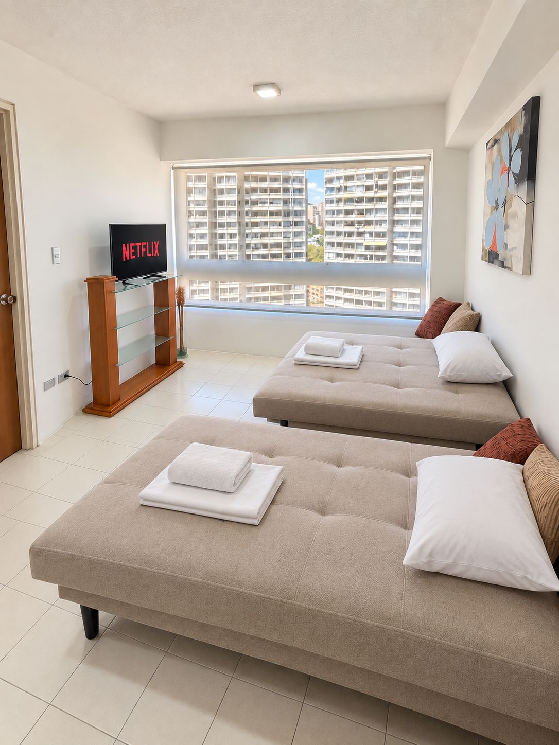 Une chambre d’hôtel avec deux canapés, une télévision et une fenêtre donnant sur des immeubles de grande hauteur.