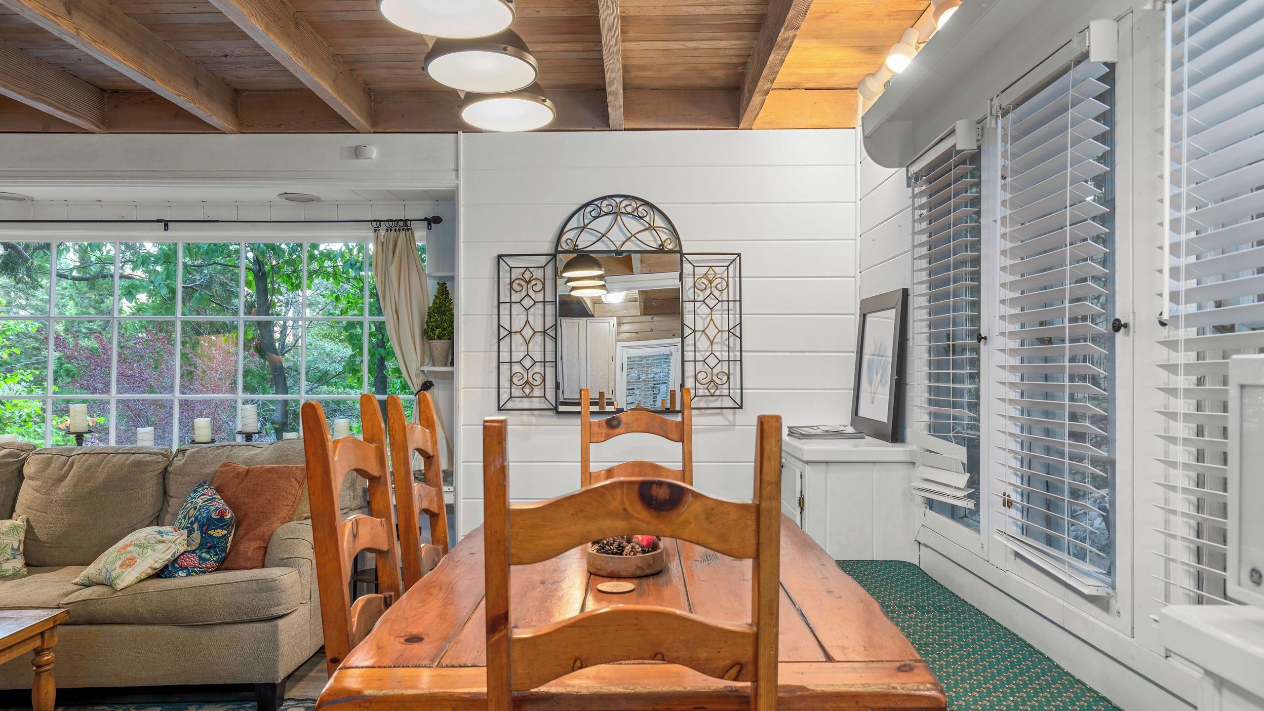 A dining area with a wooden table and chairs, a sofa with cushions, and a window with blinds.