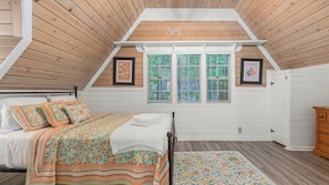 A bedroom with a sloped ceiling, a bed with floral bedding, a window with blinds, and a door with a handle. - Green Gables Cottage by Avantstay Classic Mountain Cottage Family Friendly Near Lake + Skypark (Lake Arrowhead)