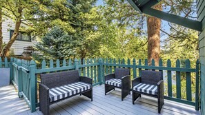 An outdoor deck with two wicker chairs and a bench, surrounded by a teal fence and trees. - Green Gables Cottage by Avantstay Classic Mountain Cottage Family Friendly Near Lake + Skypark (Lake Arrowhead)
