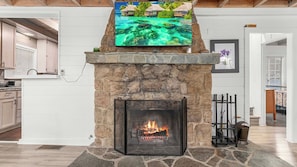 Ein Steinkamin mit einem darüber angebrachten Fernseher, ein Feuer brennt darin, und eine Steinsäule.