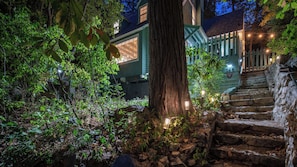 A stone staircase leading to a house with a porch, surrounded by greenery and illuminated by outdoor lights. - Green Gables Cottage by Avantstay Classic Mountain Cottage Family Friendly Near Lake + Skypark (Lake Arrowhead)
