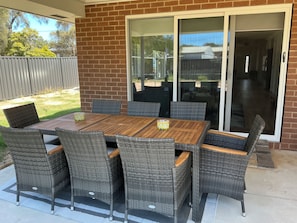 An outdoor patio with a wooden table and wicker chairs, a sliding glass door, and a brick wall.