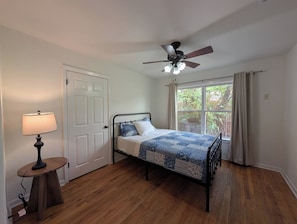 Une chambre à coucher avec un lit, un ventilateur de plafond, une fenêtre avec des rideaux et une lampe sur une table de chevet.