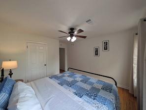 Ein Schlafzimmer mit Bett, Deckenventilator, Tür und Nachttisch mit Lampe.