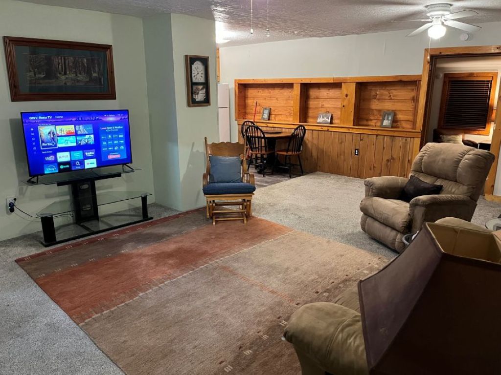 Un soggiorno con televisione a schermo piatto, un tavolo da pranzo in legno con sedie, un divano e una ventola a soffitto.