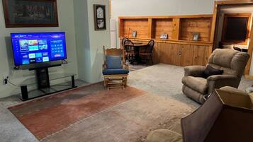 Un soggiorno con televisione a schermo piatto, un tavolo da pranzo in legno con sedie, un divano e una ventola a soffitto.