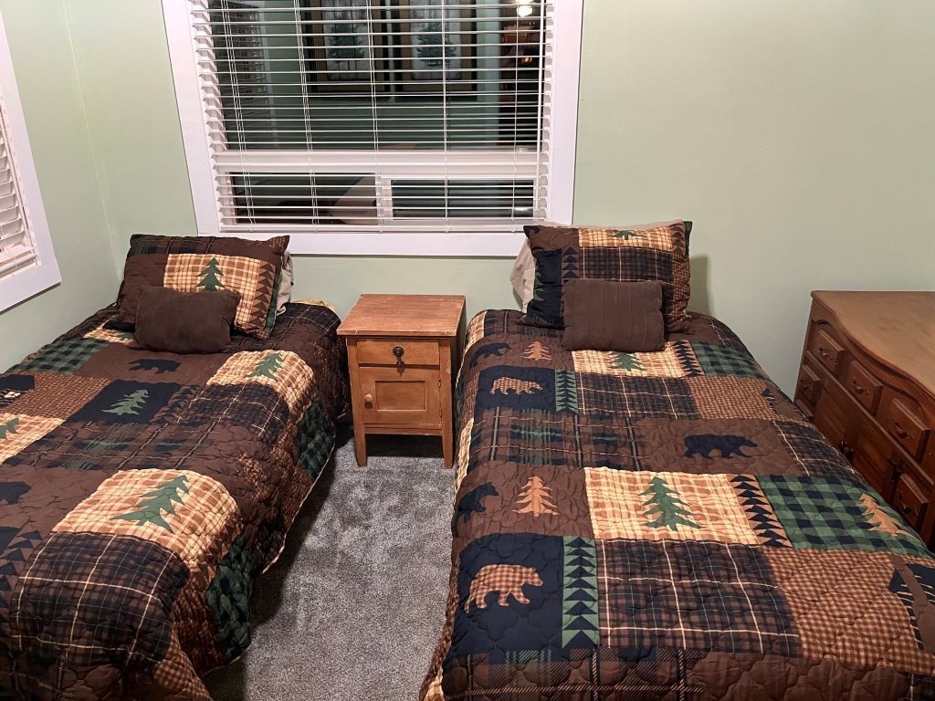 A bedroom with two beds, a nightstand, a dresser, and a window with blinds.