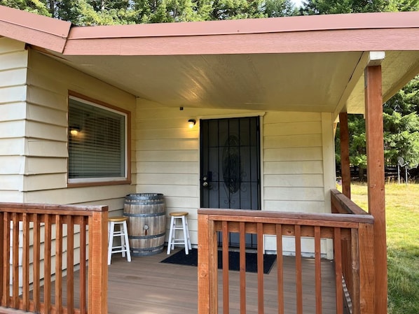 A covered porch with a wooden railing, a door, and a window with blinds.