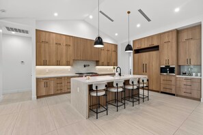 A modern kitchen with wooden cabinets, a central island with bar stools, pendant lighting, and built-in appliances.