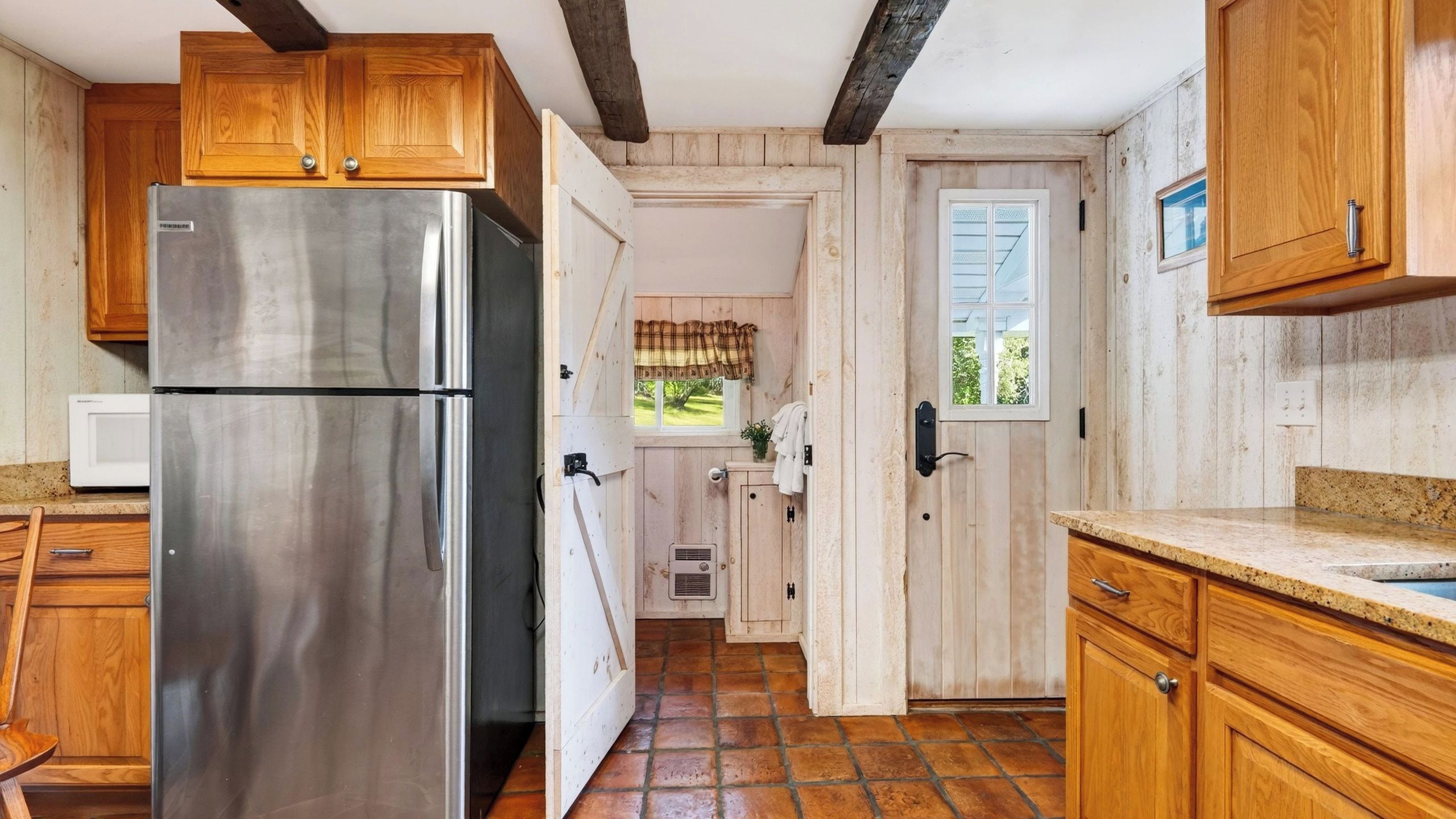 Une cuisine avec des meubles en bois, un réfrigérateur en acier inoxydable et une fenêtre donnant sur un paysage verdoyant.