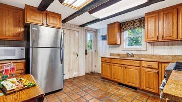 A kitchen with wooden cabinets, a stainless steel refrigerator, a microwave, and a tiled floor.