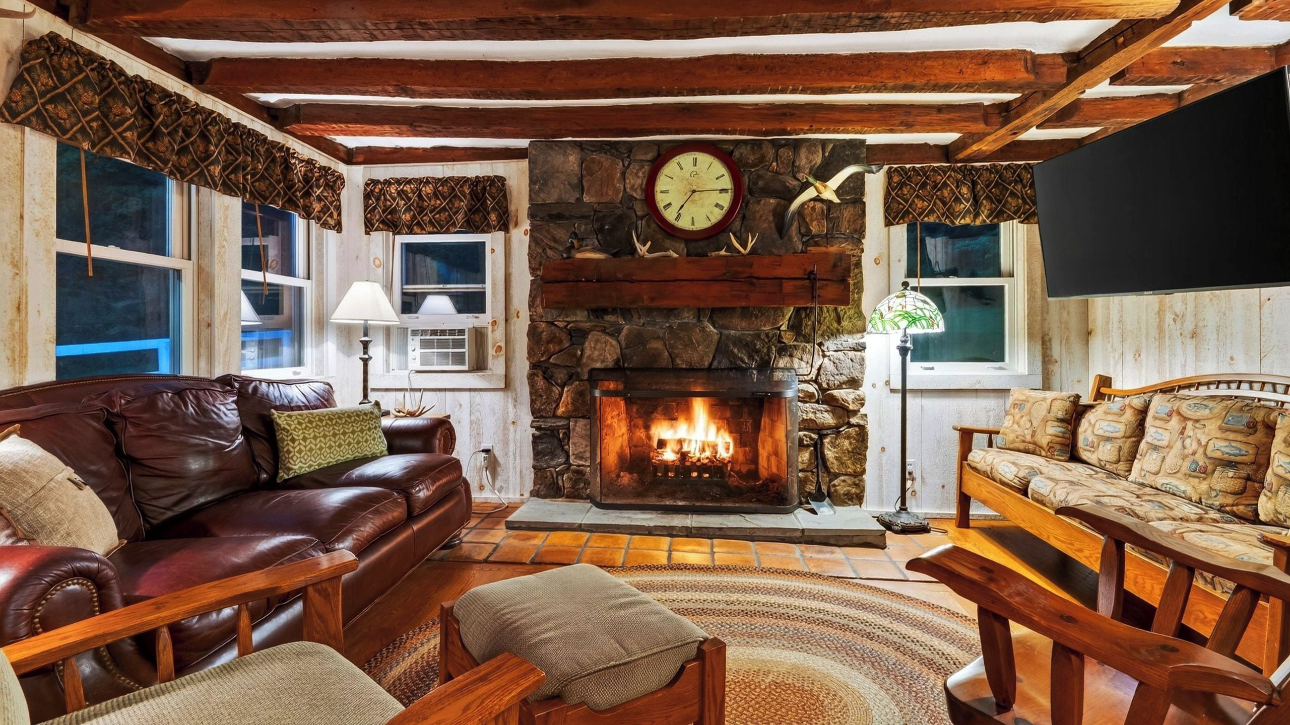 A cozy living room with a stone fireplace, leather sofas, and wooden beams on the ceiling.