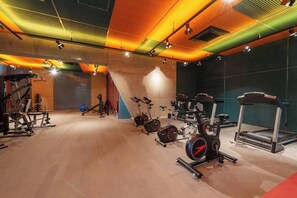 A gym with various exercise equipment, including treadmills and stationary bikes, and a wall with soundproofing panels. - Setin_2302 · Studio no 23º andar | 1 min do Metrô República (Santa Ifigênia)