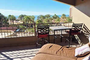 Ein Balkon mit Tisch und Stühlen, der Blick auf einen Strand und Palmen freigibt.