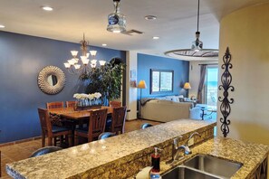A modern kitchen with granite countertops, a dining area with a wooden table and chairs, and a living room with a sofa and a view of the outdoors. - Elevated Bella Sirena Views: 2nd Floor Luxury (Puerto Peñasco)