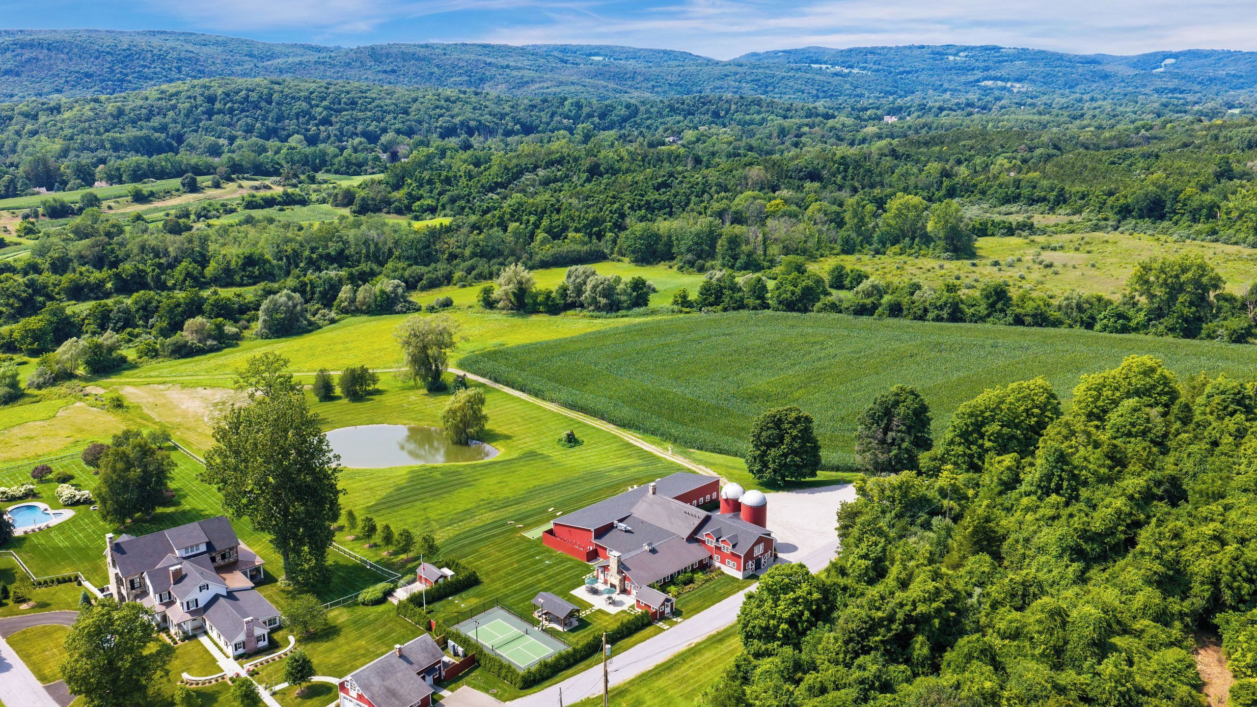 An aerial view of a rural property with a large field, a pond, and a red barn.