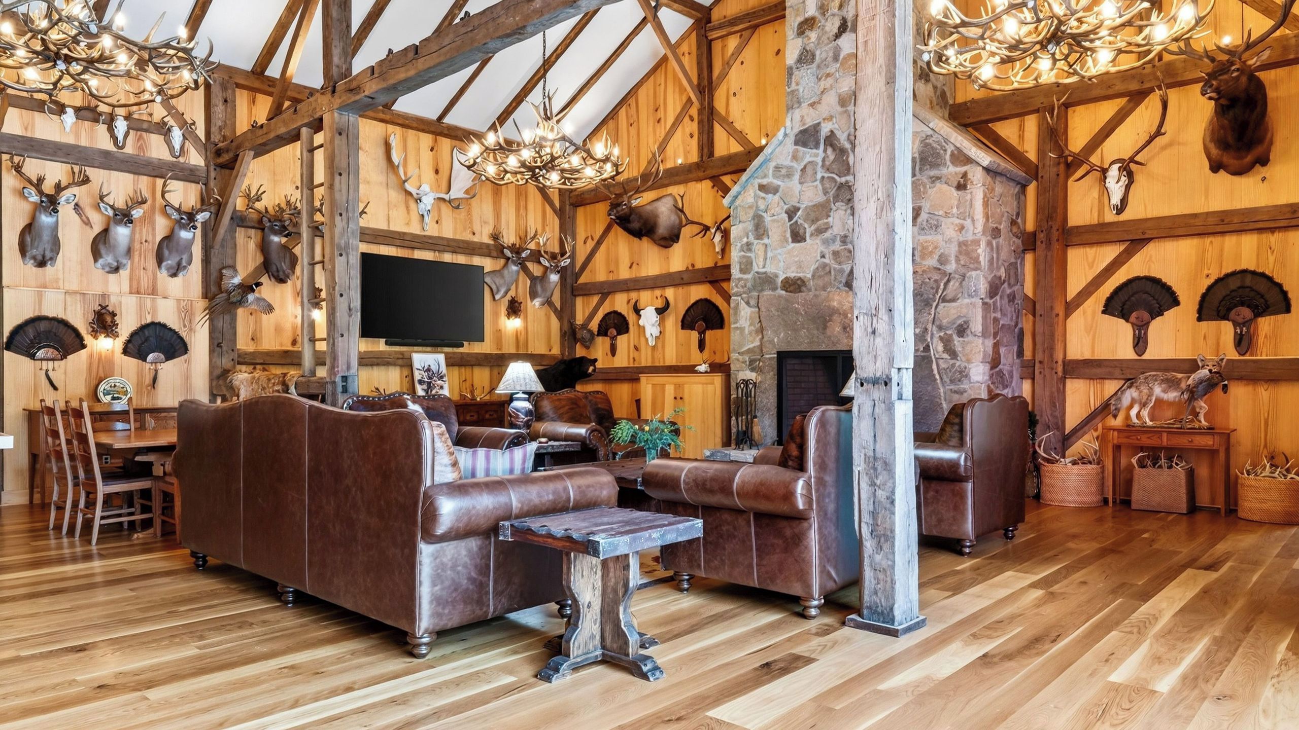 A rustic interior with a stone fireplace, leather furniture, and various animal skulls mounted on the walls.