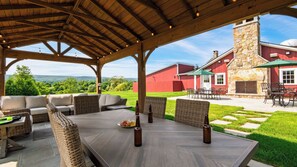 An outdoor patio with a covered seating area, a dining table, and a stone building in the background. - The Bear Barn by Avantstay 150-acre Historic 1860 Barn Fire Pit + Mountain Views (Dover Plains)
