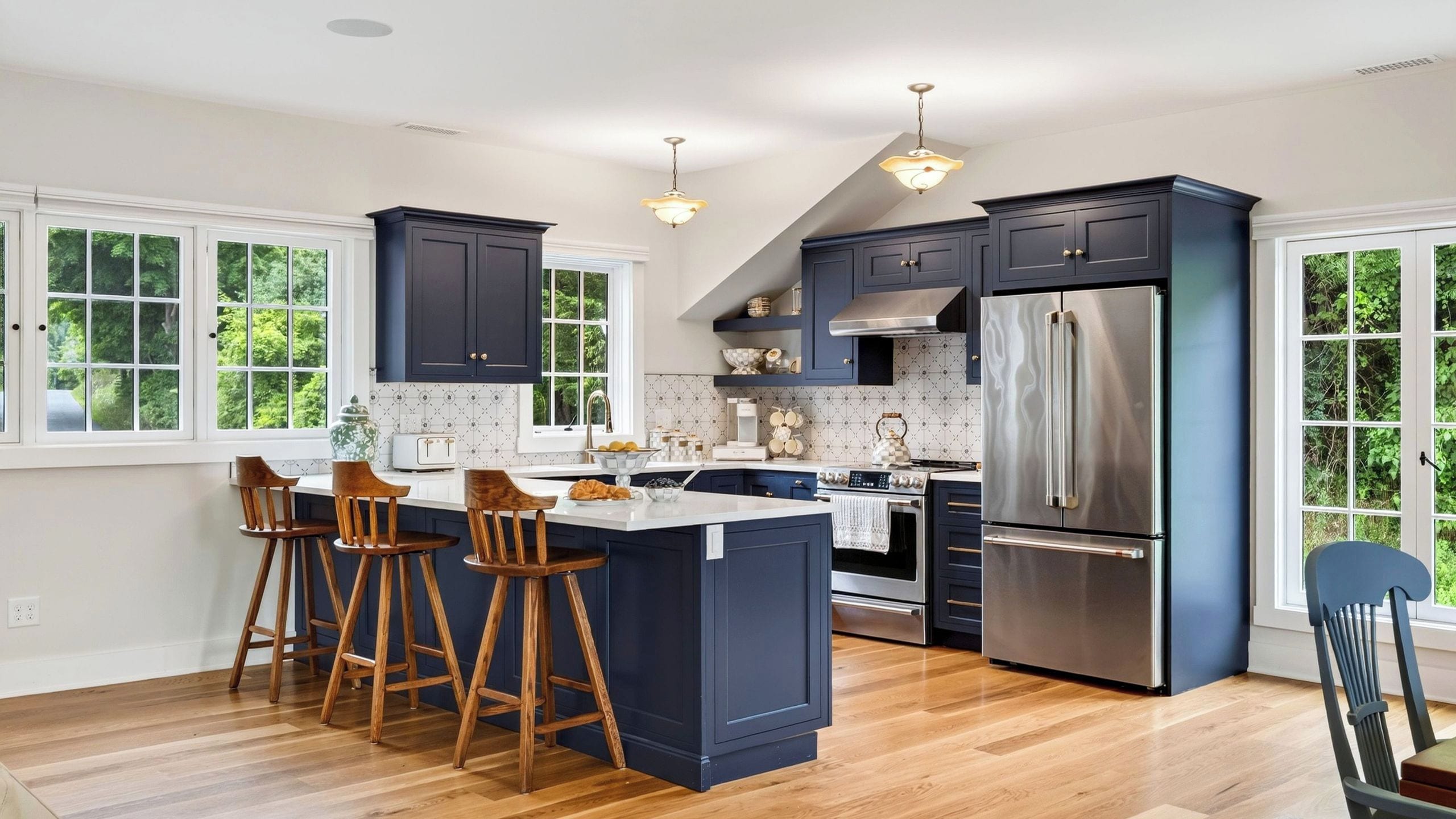 A modern kitchen with a central island, bar stools, a stainless steel refrigerator, and a large window.