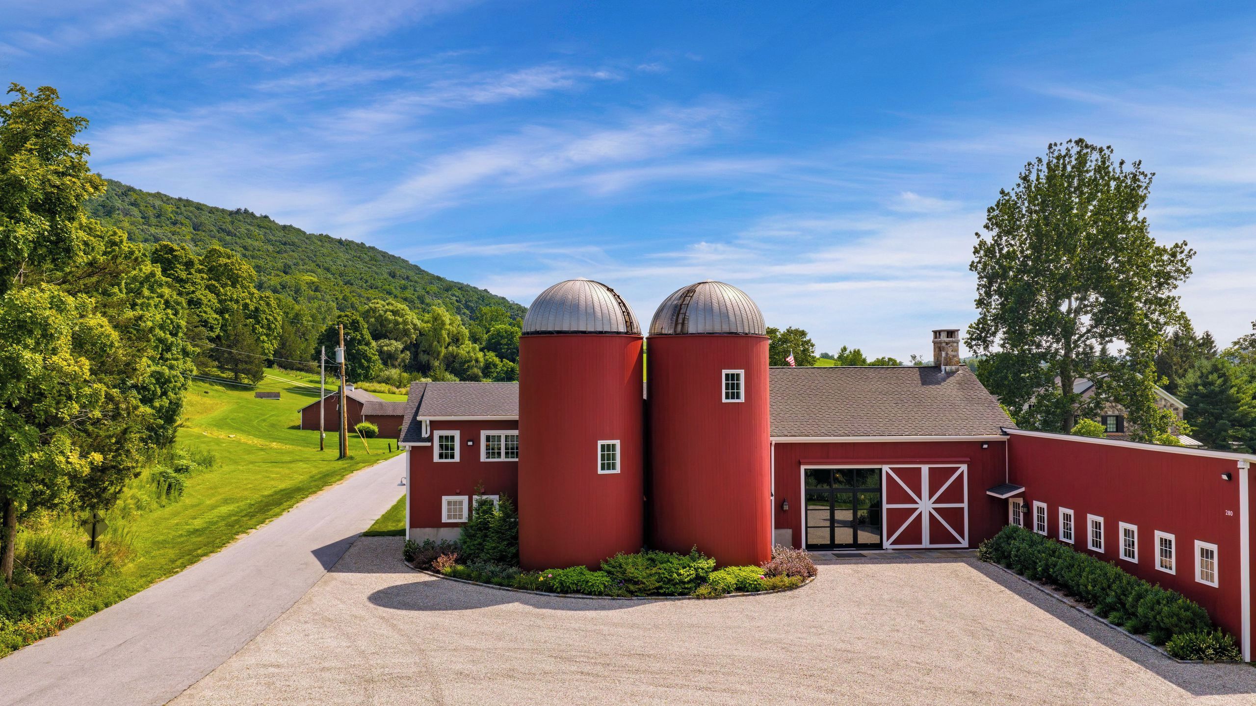 A red barn with two silos, a gravel driveway, and a green landscape.