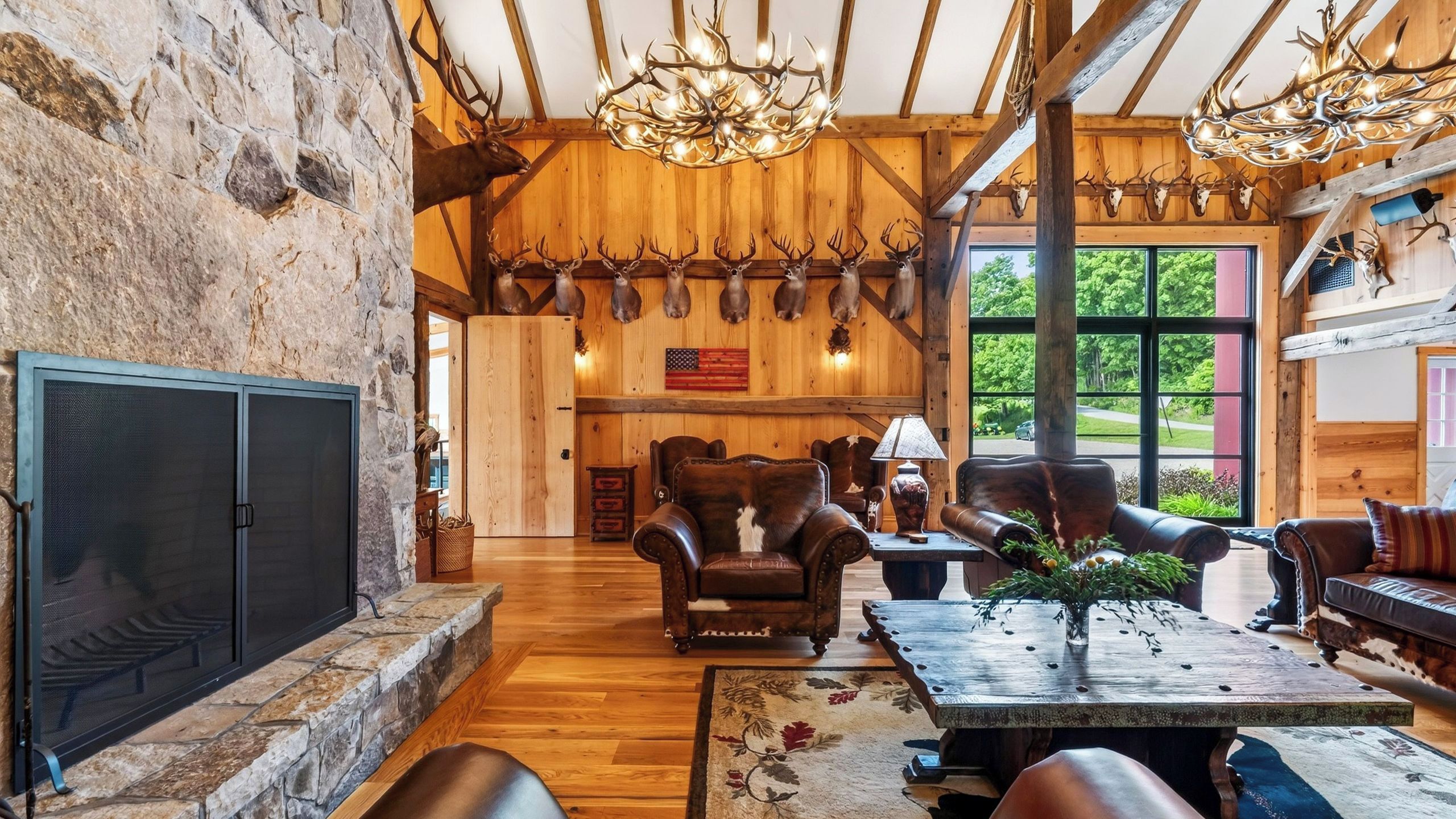 A rustic interior with stone walls, wooden beams, a fireplace, leather furniture, and antler decorations.