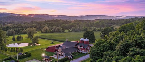 A rural landscape with a large barn, a tennis court, and a pond.