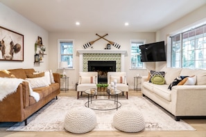 A living room with a fireplace, two sofas, a coffee table, and a flat-screen TV mounted on the wall. - Painted Bear - Hot Tub • Pet Friendly • Quiet & Centrally Located • Fireplace (Big Bear)