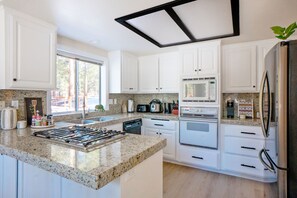 A modern kitchen with white cabinets, granite countertops, a built-in stove, a microwave, and a refrigerator. - Painted Bear - Hot Tub • Pet Friendly • Quiet & Centrally Located • Fireplace (Big Bear)