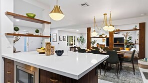 A modern kitchen with a large island, pendant lighting, and a dining area with a wooden table and chairs. - The Royal Palms by Avantstay Pool + Hot Tub + Game Room + Fire Pit (Palm Springs)