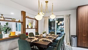 Un espace repas avec une table en bois, des chaises à l’assise rembourrée de tissu vert et des lampes suspendues.