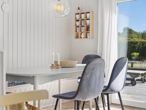 A dining area with a white table, two grey chairs, a hanging light fixture, and a shelf with decorative items. - "Henryka" - 750m from the sea by Interhome (Gilleleje)