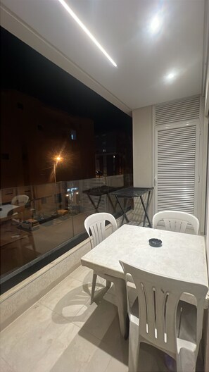 Ein Balkon mit Esstisch und Stühlen, einer Glastrennwand und Blick auf die nächtliche Stadtlandschaft.