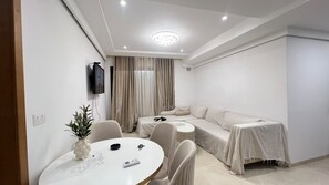 Ein moderner, gut beleuchteter Raum mit einer Couch, einem Esstisch mit Stühlen und einem an der Wand montierten Fernseher.