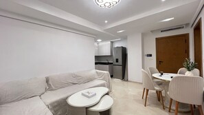 Un espacio habitable moderno con sofá, una mesa de comedor redonda y una zona de cocina al fondo.