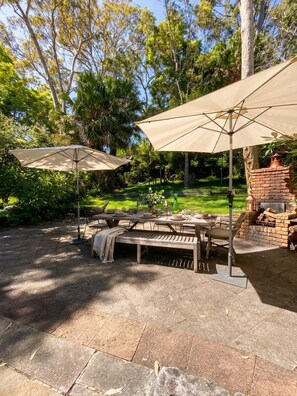 An outdoor patio with a stone table, two umbrellas, and a brick fireplace. - Avalon home flat 5 minute stroll to village (Avalon Beach)