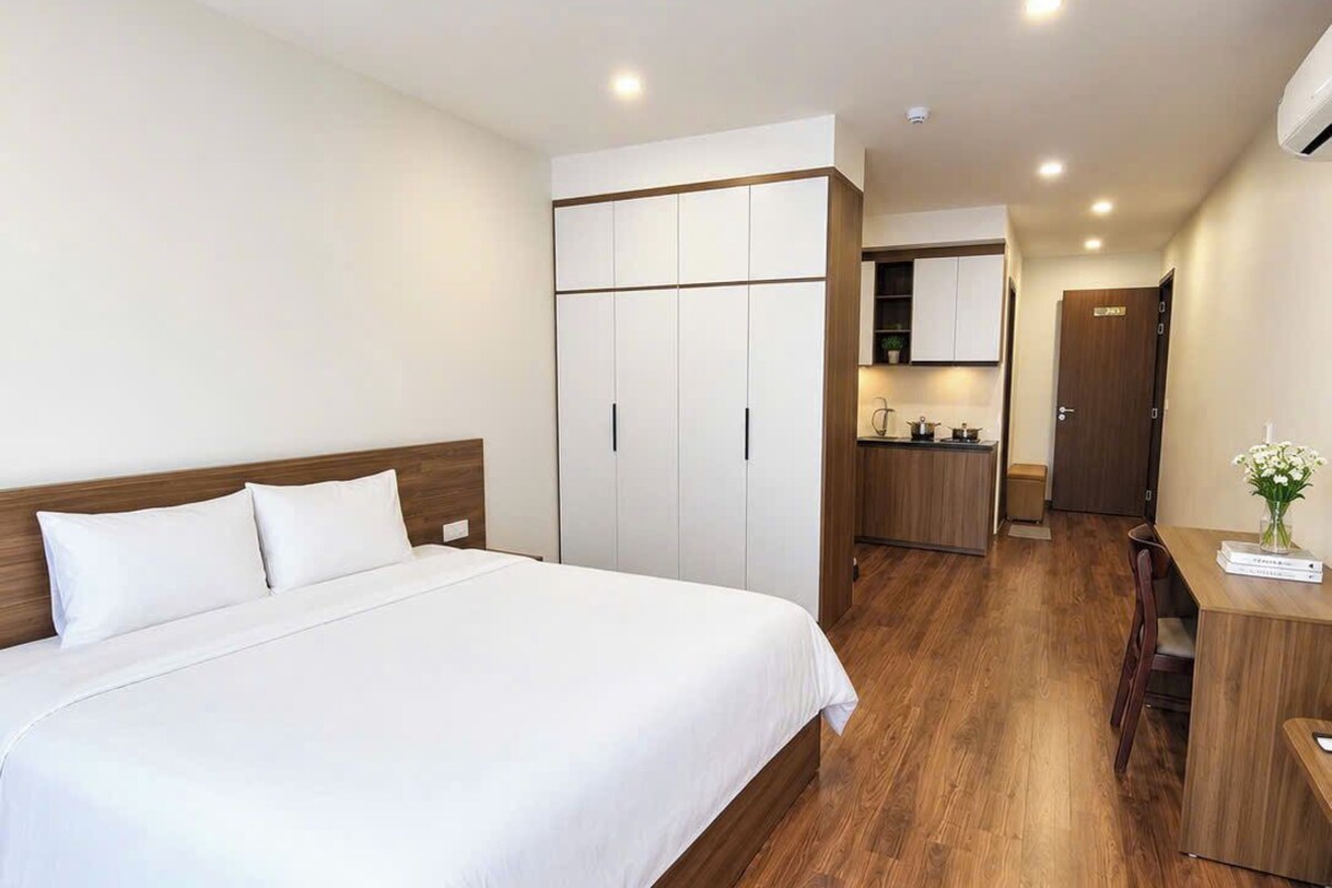 A hotel room with a large bed, wooden flooring, a kitchenette, and a desk.