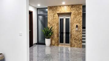 A modern lobby with a marble floor, an exit sign, a potted plant, and an elevator.